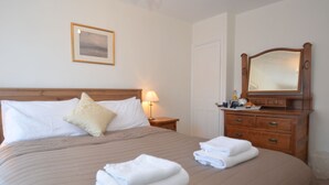 A neatly made bed with pillows, a bedside lamp, a dresser with a mirror, and a framed picture on the wall. - Crown Cottage (Rye)