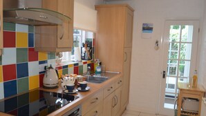 A kitchen with wooden cabinets, a colorful backsplash, a stove, and a sink. - Crown Cottage (Rye)