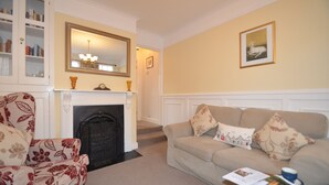 A living room with a fireplace, a sofa, a chair, and a bookshelf. - Crown Cottage (Rye)