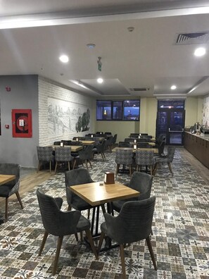 Un restaurant avec de nombreuses tables et chaises, un sol à motifs et une fresque murale.