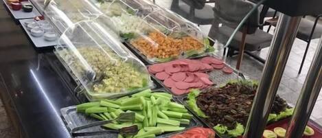 A buffet with various food items including sliced tomatoes, green beans, and other vegetables.