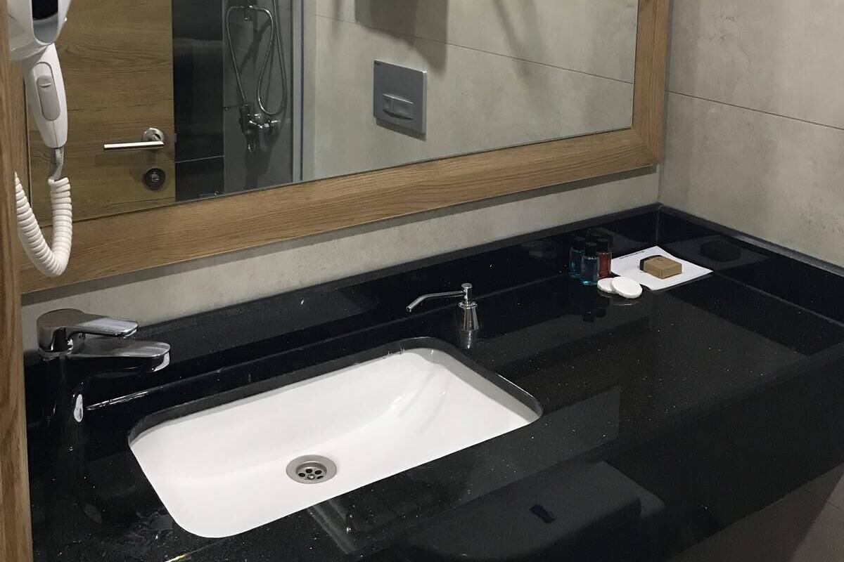A modern bathroom with a large mirror, a black countertop, a white sink, a shower, and a towel rack.
