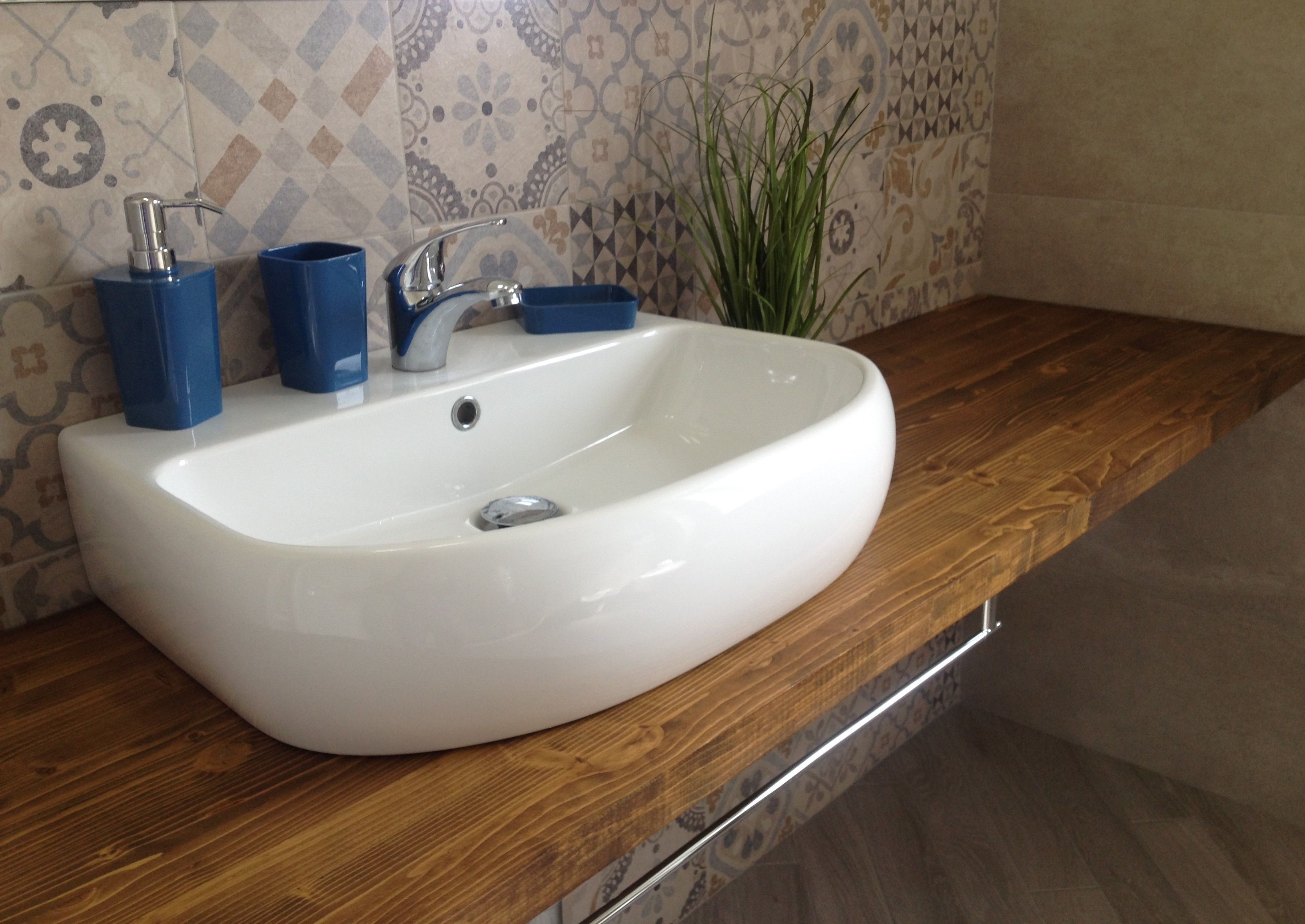 A white sink with a modern faucet, blue soap dispensers, and a potted plant on a wooden countertop.