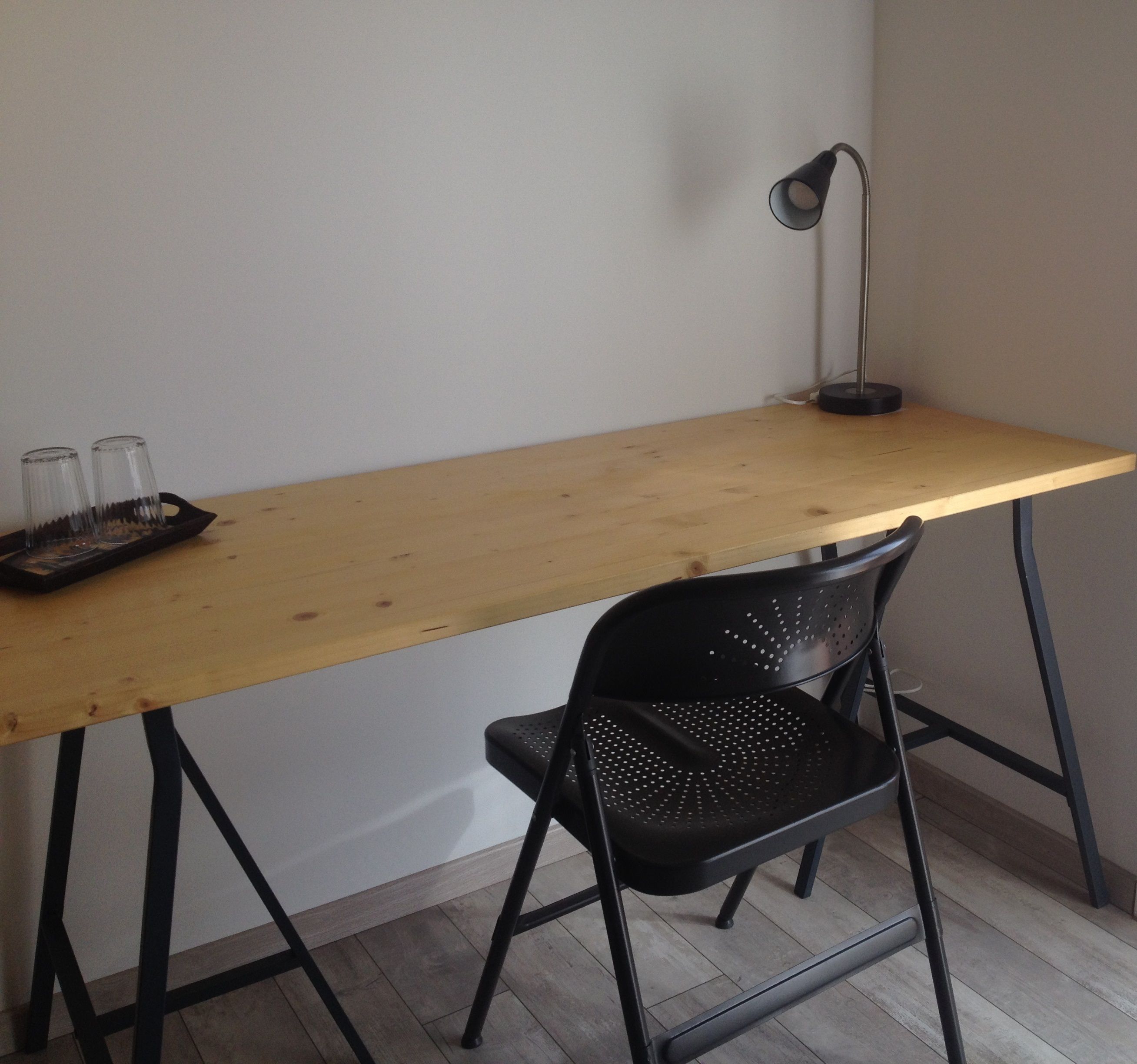 A wooden desk with a black chair, a lamp, and two glasses on a tray.