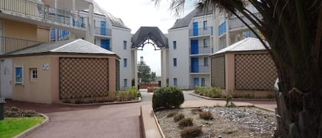 A residential building with a central entrance, multiple balconies, and a gated entrance.