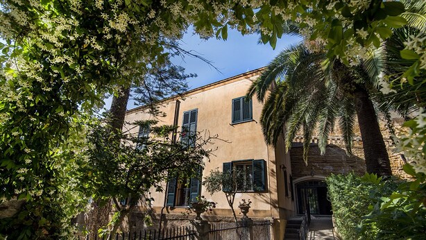 Un bâtiment doté d’une façade en pierre, de volets verts et d’une entrée fermée par un portail.
