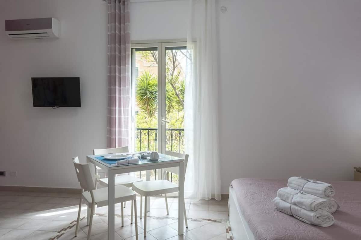 A room with a bed, a table with chairs, a TV, and a balcony with curtains.