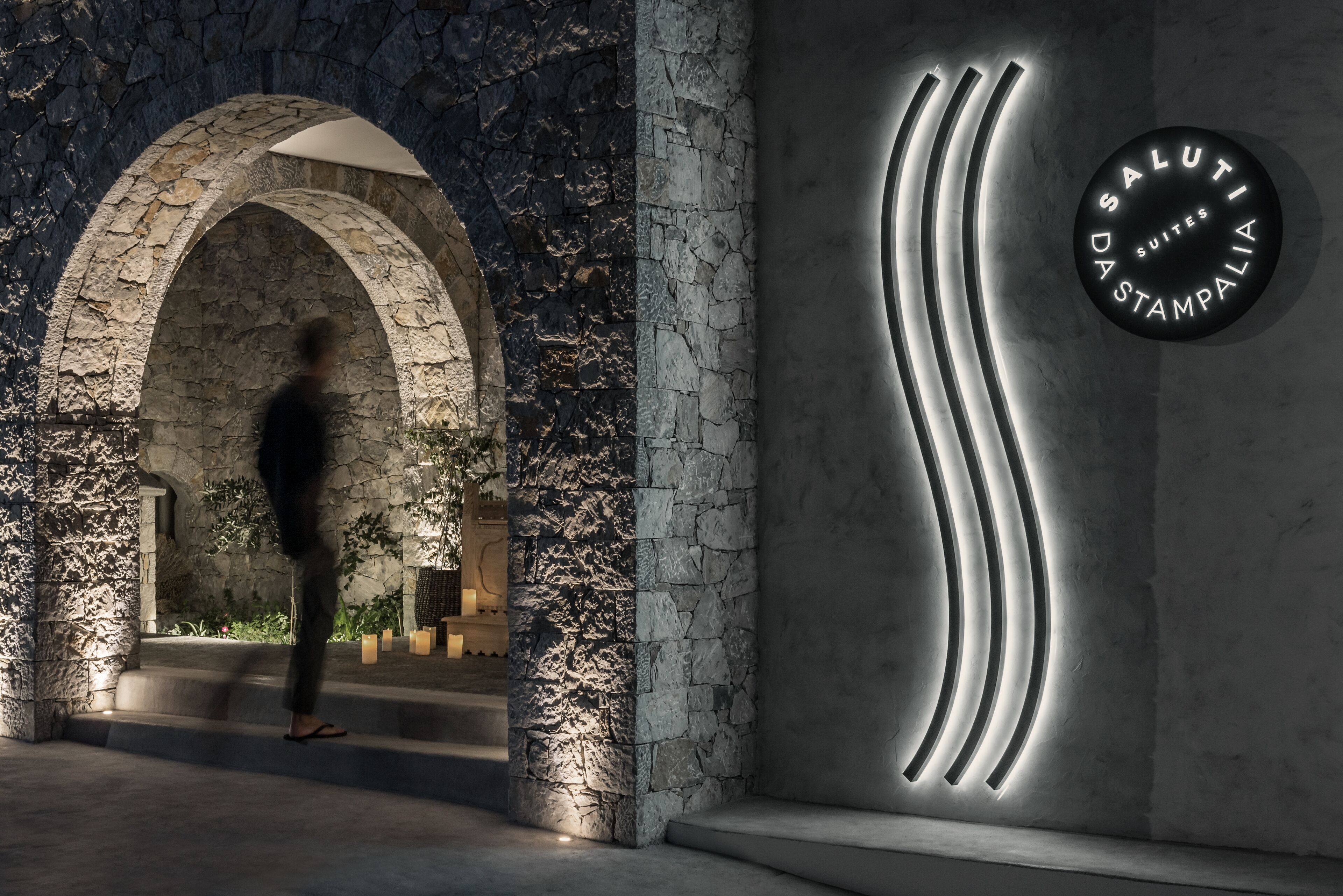 A stone archway leading to a building with a sign that reads "DASALUTI SUITES STAMPALIA".