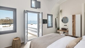 A bedroom with a large bed, a bedside table, a mirror, a window with a view of the sea, and a door leading to an outdoor balcony.