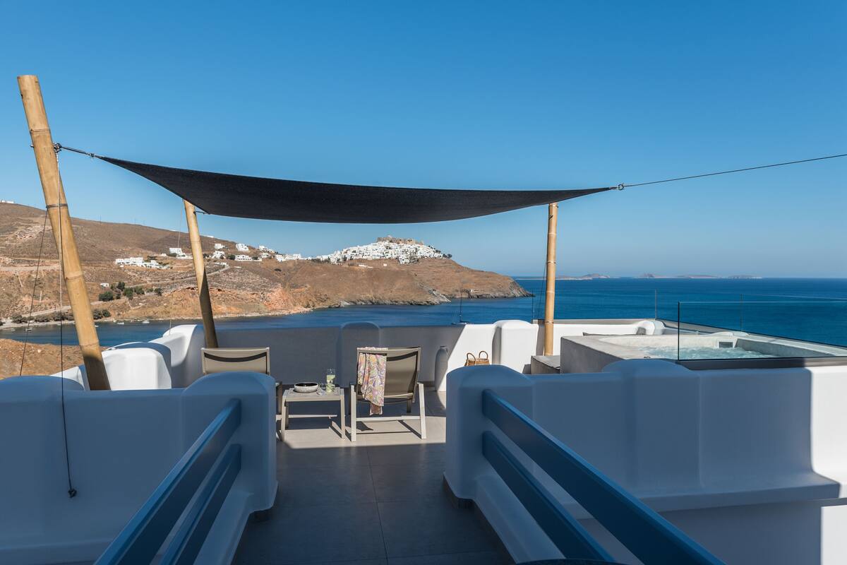 Un espace extérieur ensoleillé, aménagé avec des sièges, d’où l’on peut admirer la mer et une colline au loin.