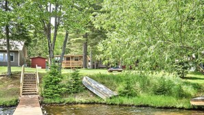 A wooden dock leading to a house with a red exterior, surrounded by lush greenery and trees.