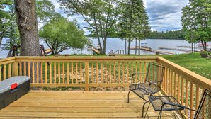 A wooden deck with metal chairs and a red toolbox, overlooking a lake with docks and boats.