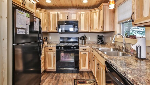 A kitchen with wooden cabinets, a black refrigerator, a microwave, a stove, and a sink.