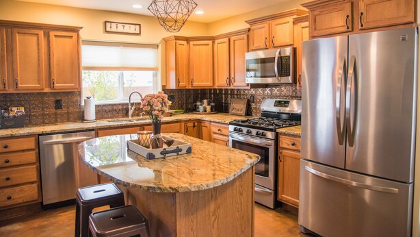 Una cocina moderna con armarios de madera, electrodomésticos de acero inoxidable, una isla central y una lámpara colgante.