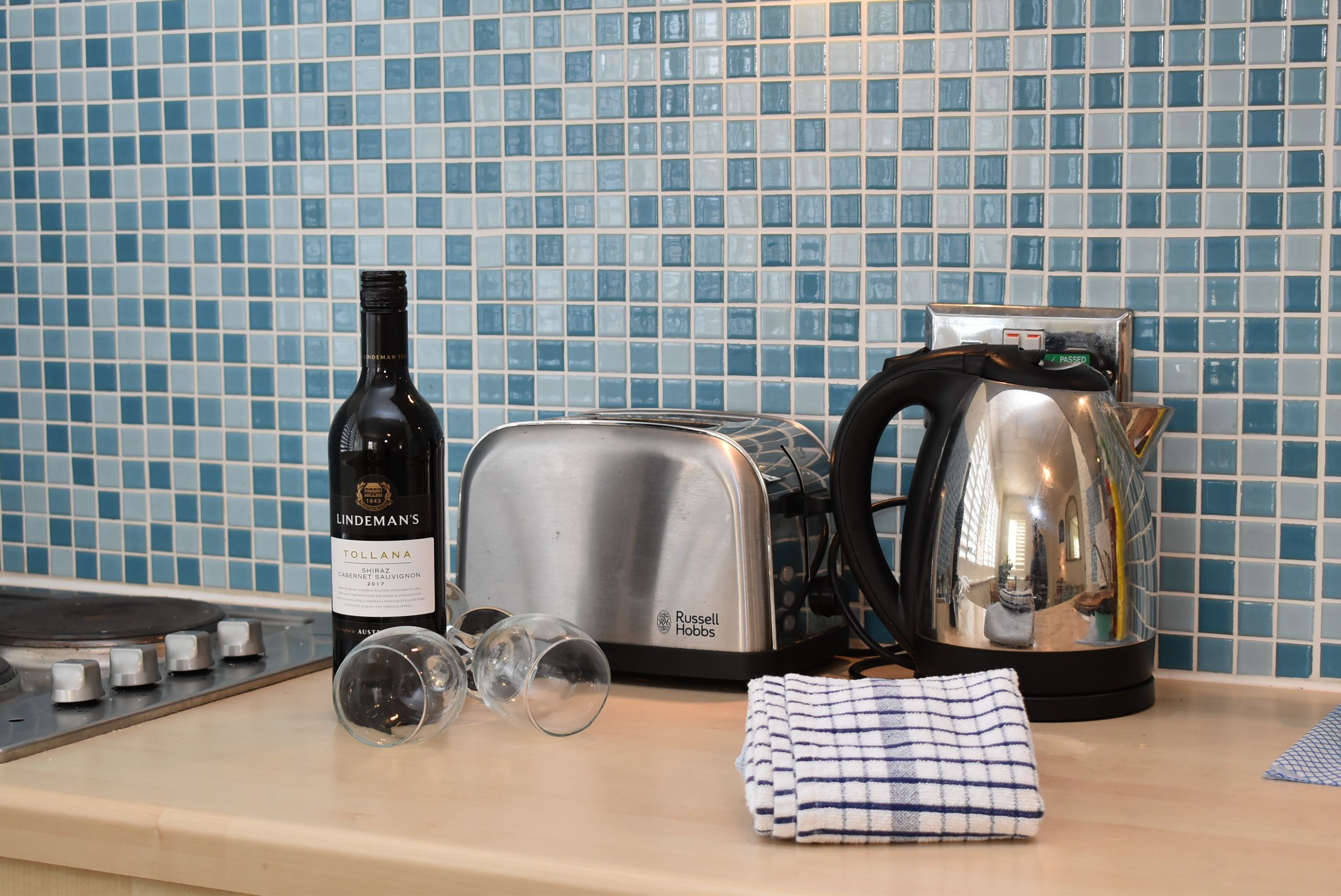 Uma bancada de cozinha com uma garrafa de Lindeman's Tolland Chardonnay, uma torradeira, uma chaleira e um pano dobrado.