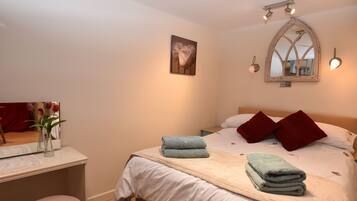 Un dormitorio con cama, una mesita de noche con un florero, un espejo e iluminación en la pared.