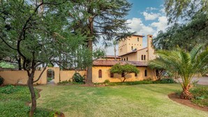 A building with a tiled roof and arched windows, surrounded by a well-maintained lawn and trees. - Airport Tower Lodge (Kempton Park)