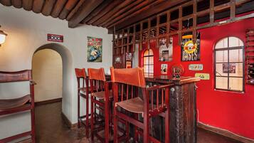 A bar area with wooden chairs and a bar counter, red walls, and various posters and signs.