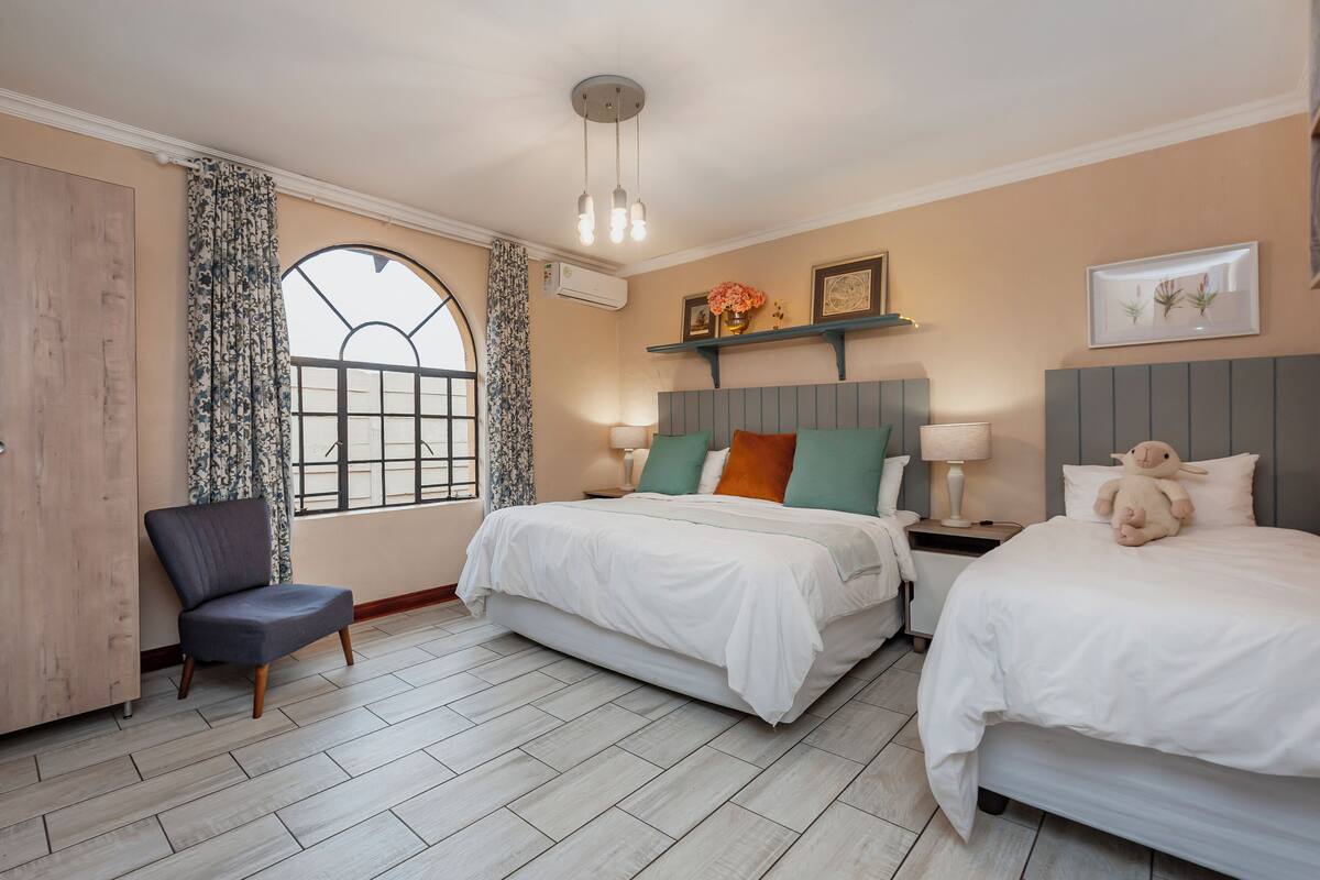 A hotel room with two beds, a chair, a desk, and a window with curtains.