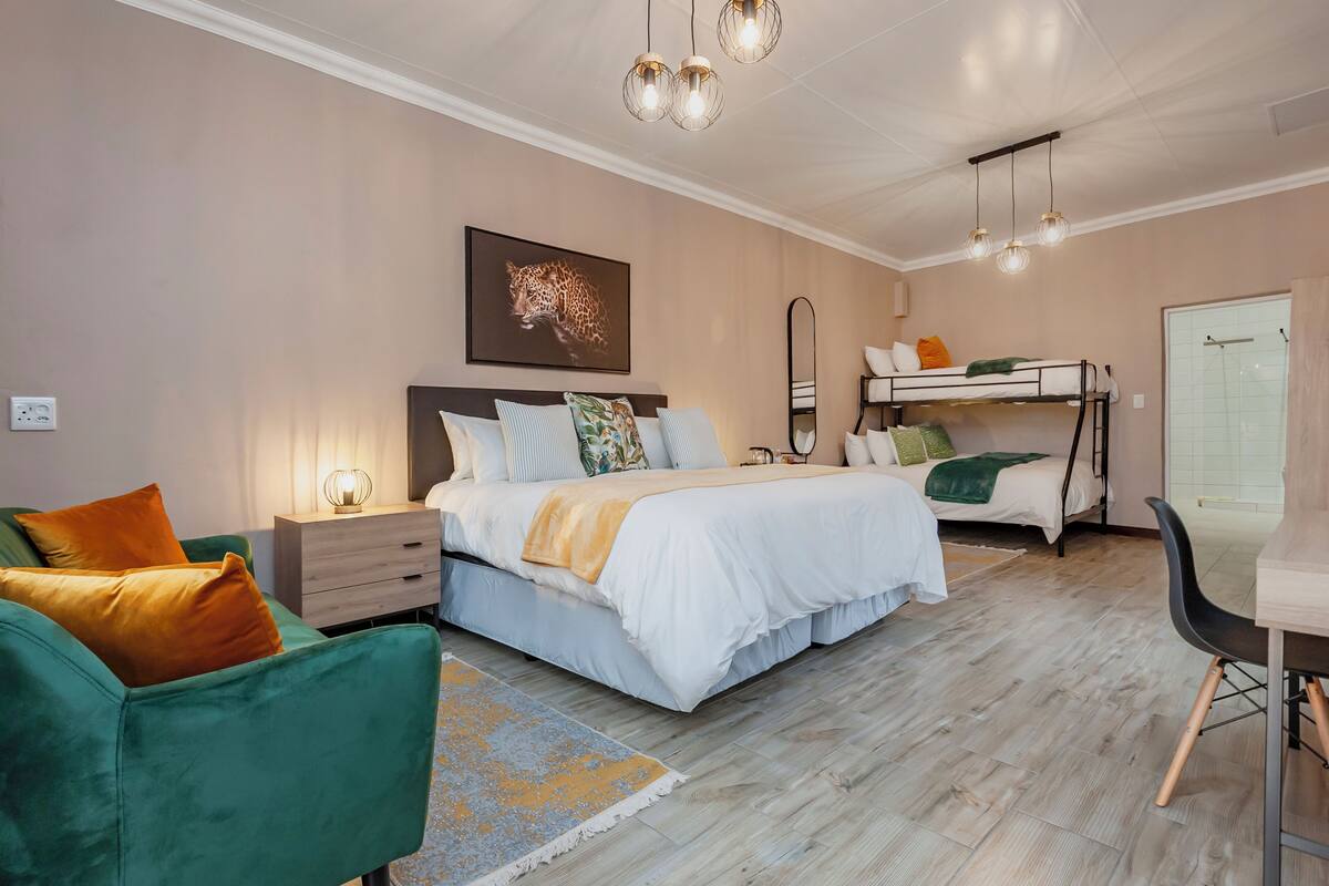 A modern bedroom with a large bed, a bunk bed, a green armchair, a bedside table, and a wall-mounted mirror.