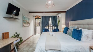 A modern bedroom with a large bed, a TV, a desk, and a view of the street through a glass door. - Airport Tower Lodge (Kempton Park)