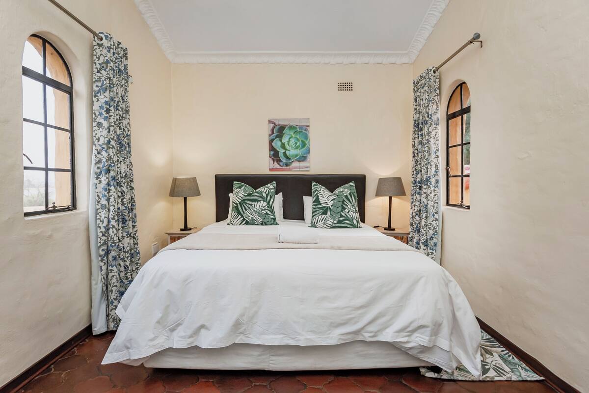 A neatly made bed with a white bedspread and two pillows, flanked by two bedside lamps.