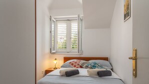 Ein ordentlich bezogenes Bett mit Kopfteil, Nachttischlampe und einem Fenster mit Jalousien.