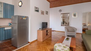 Ein kompakter Wohnraum mit Küchenbereich, einer Holz-Unterhaltungseinrichtung inklusive Fernseher, einem Esstisch, einer Couch und einem Spiegel, der den Raum widerspiegelt.
