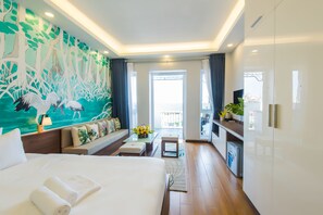 Une chambre d’hôtel avec un grand lit, un coin salon comprenant un canapé et une petite table, un tableau au mur et une vue sur l’extérieur par une fenêtre.
