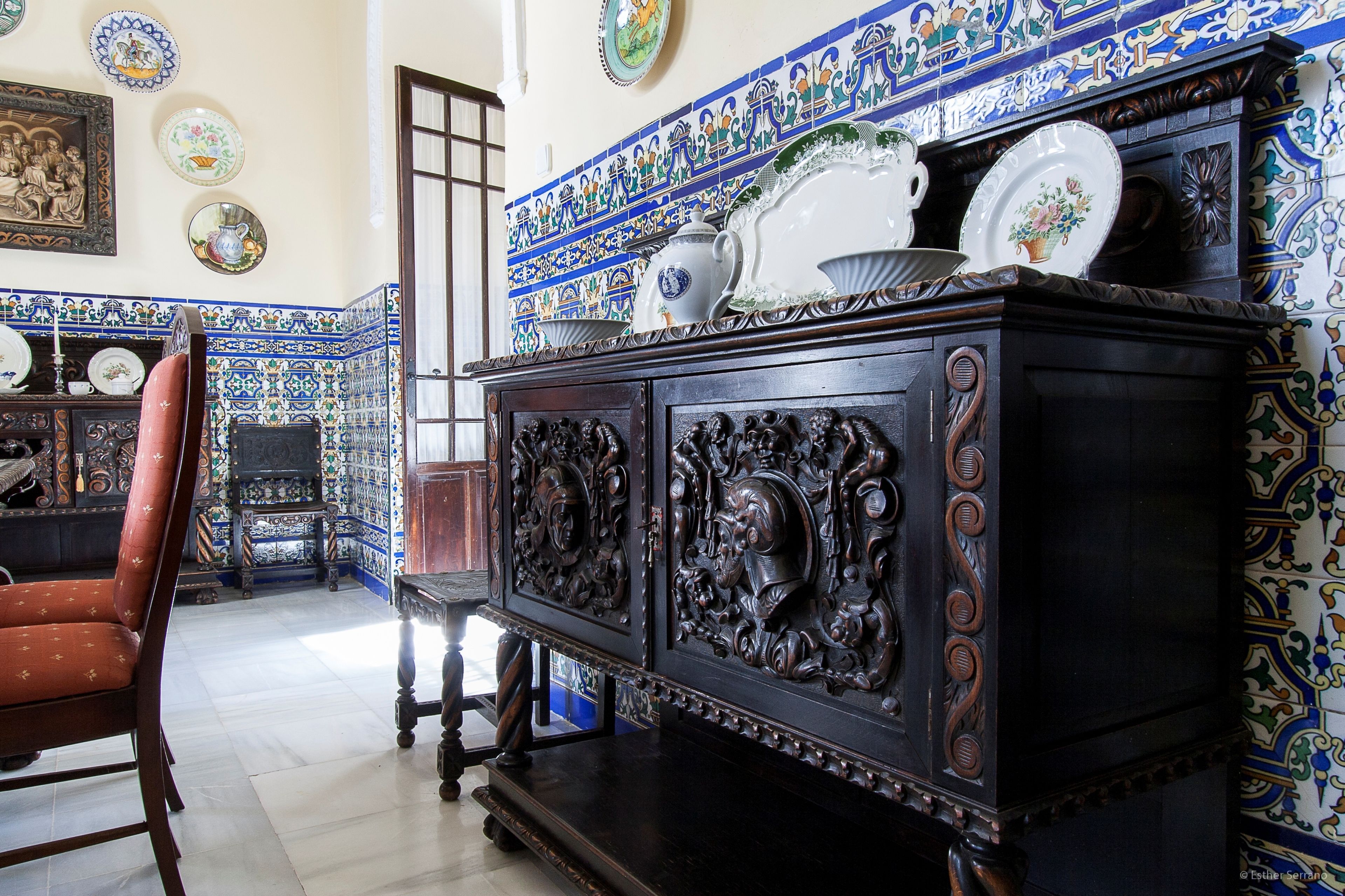 Quarto com um armário de madeira escura e entalhes elaborados, uma poltrona estofada vermelha e um revestimento de azulejos com padrões azuis e brancos.