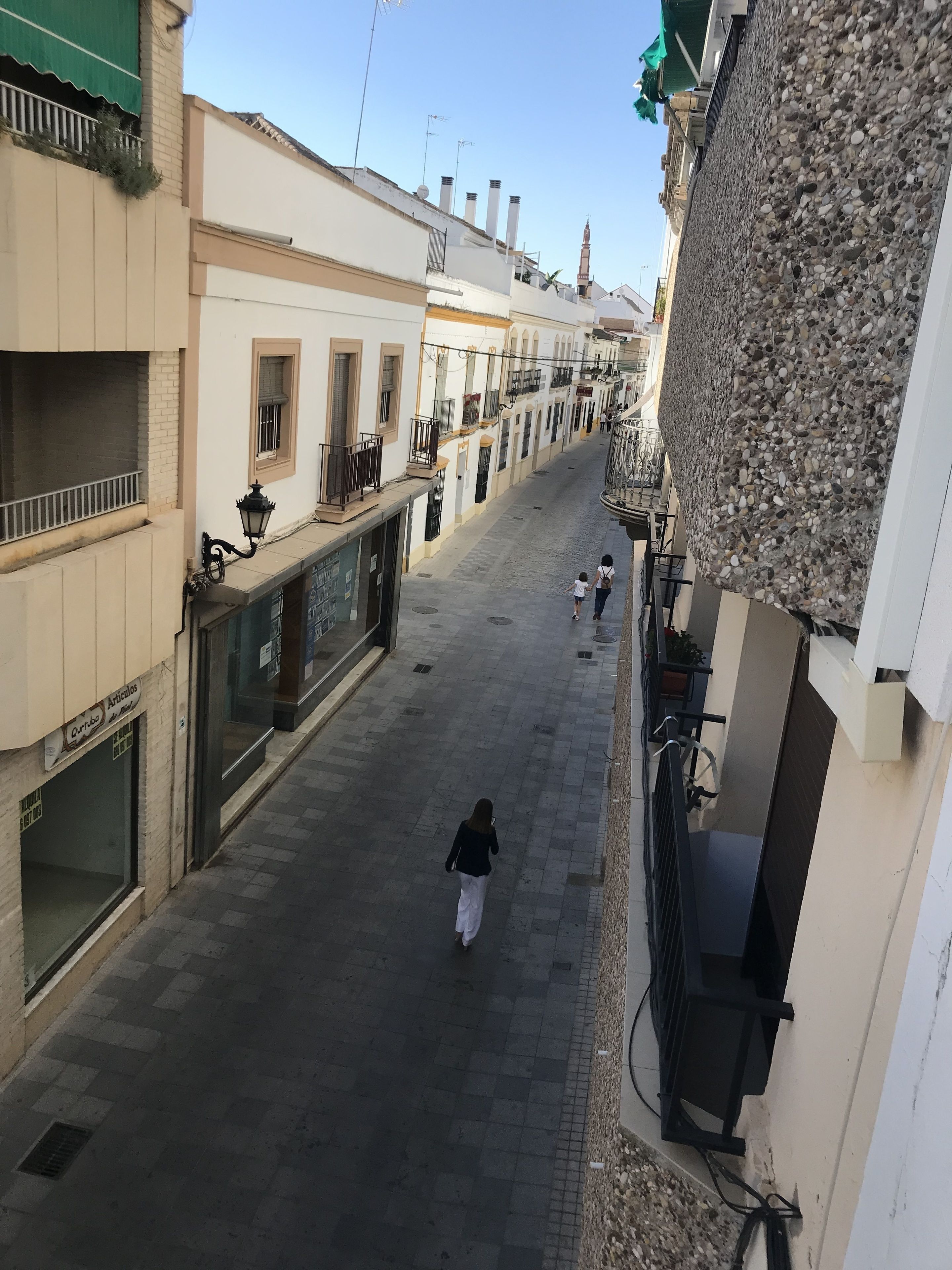 A narrow street lined with buildings, some with balconies and shops on the ground floor.