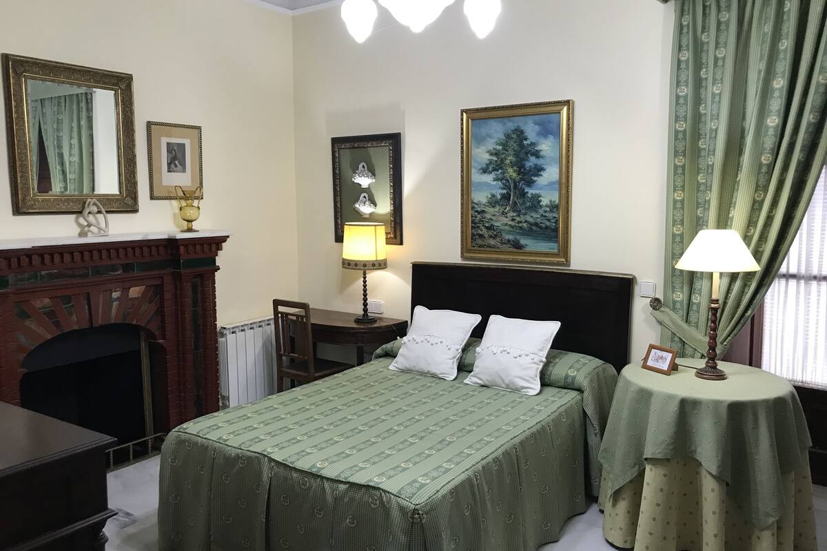 Une chambre à coucher avec un lit, une table de chevet, une lampe, une cheminée et un tableau au mur.