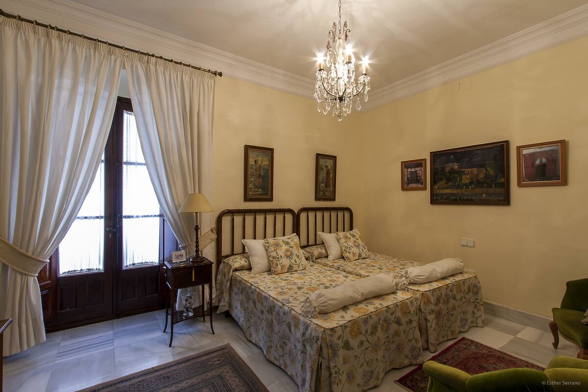 Une chambre à coucher avec un lit double, une table de chevet, une chaise, un lustre et des œuvres d’art accrochées aux murs.