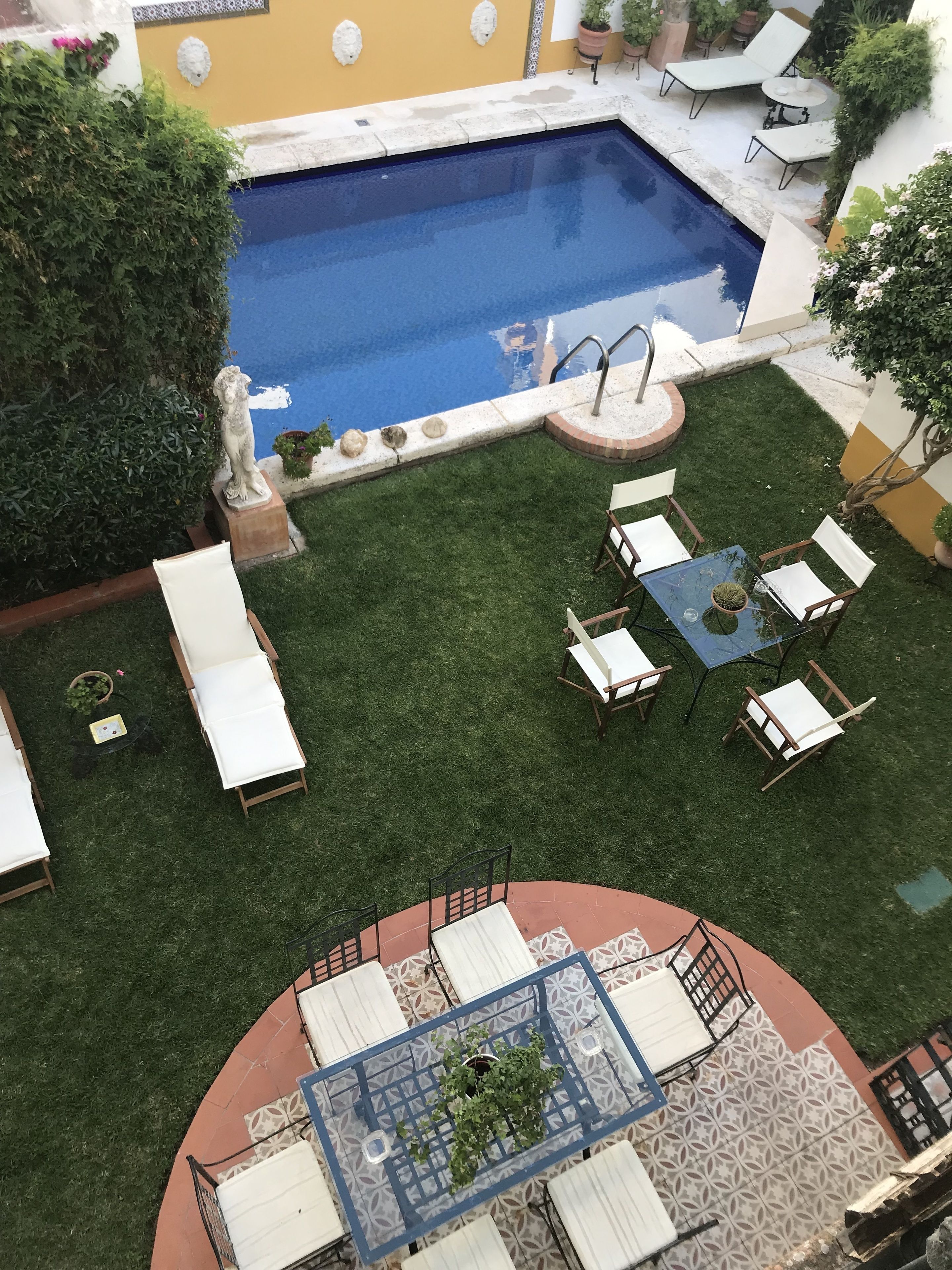 A rooftop pool area with a small statue, lounge chairs, and a table with chairs.