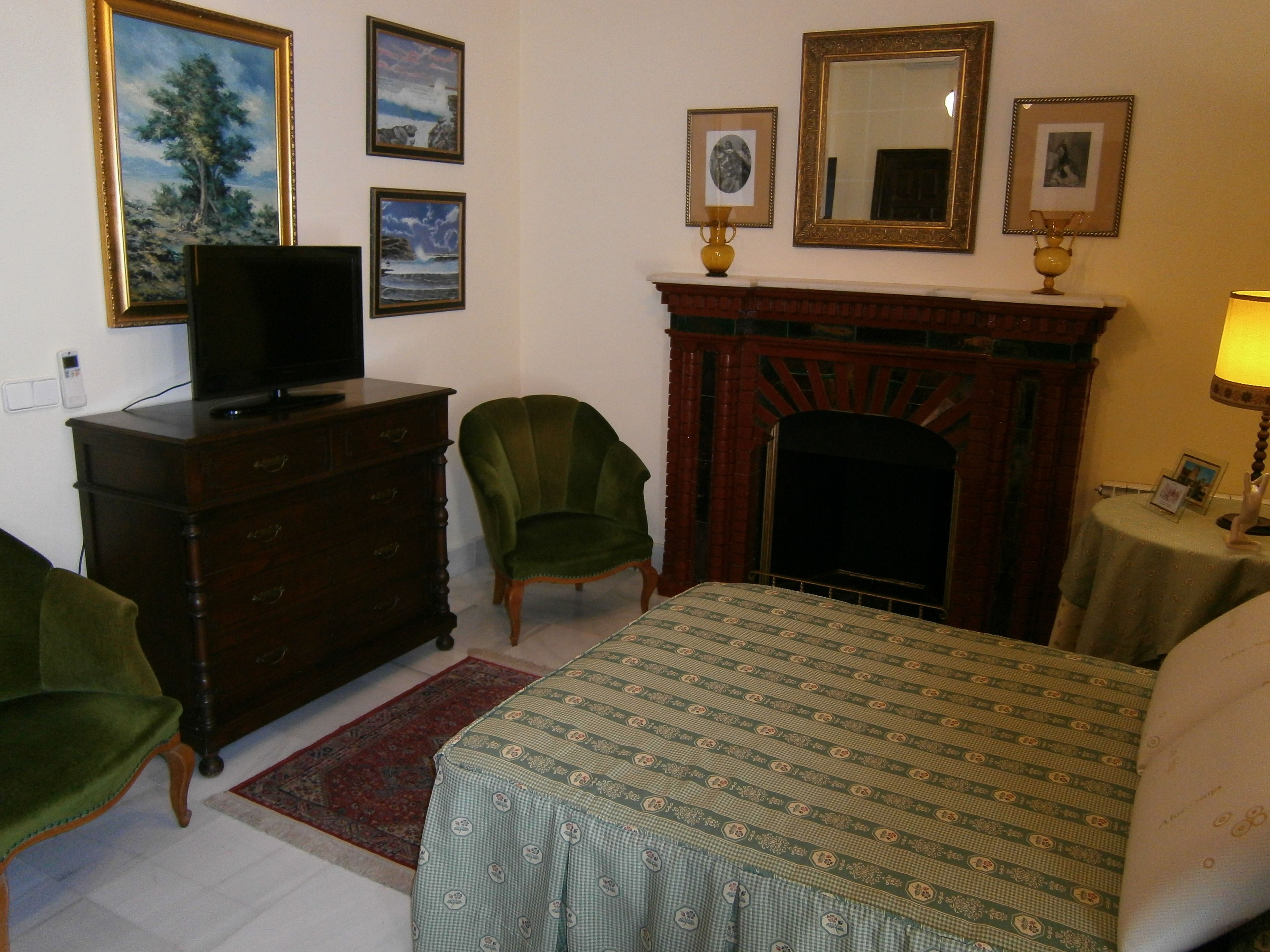 A hotel room with a bed, a dresser, a television, a fireplace, and several framed pictures on the wall.