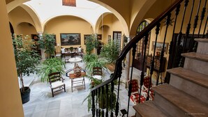 A spacious interior with a central courtyard, featuring a staircase, seating areas, and potted plants. - Casa San José (Palma del Rio)