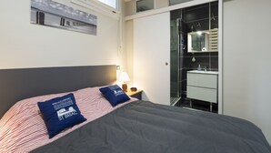 A hotel room with a bed, a nightstand, a lamp, a bathroom with a mirror, and a window.