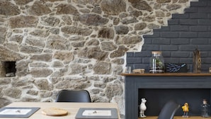 A stone wall with a fireplace, a wooden table with chairs, and decorative items on the mantel.