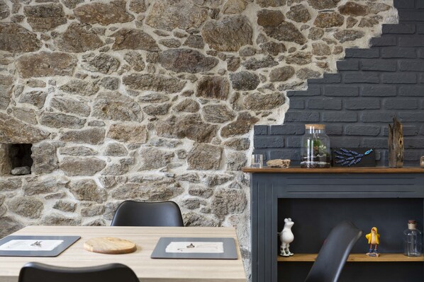 A stone wall with a fireplace, a wooden table with chairs, and decorative items on the mantel. - Very nice apartment in Paramé (Saint-Malo)