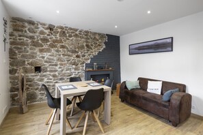 Ein gemütliches Wohnzimmer mit Steinwand, Kamin, Esstisch mit Stühlen und braunem Sofa mit Kissen.