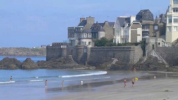 A beach with people, a stone wall, and buildings in the background.