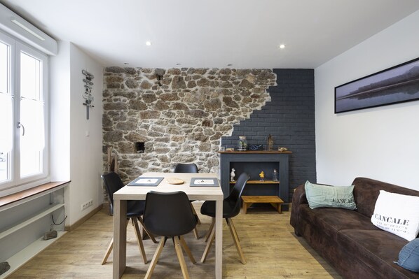 Ein gemütliches Wohnzimmer mit Steinwand, Kamin, einem Esstisch mit Stühlen und einem braunen Sofa mit Kissen.