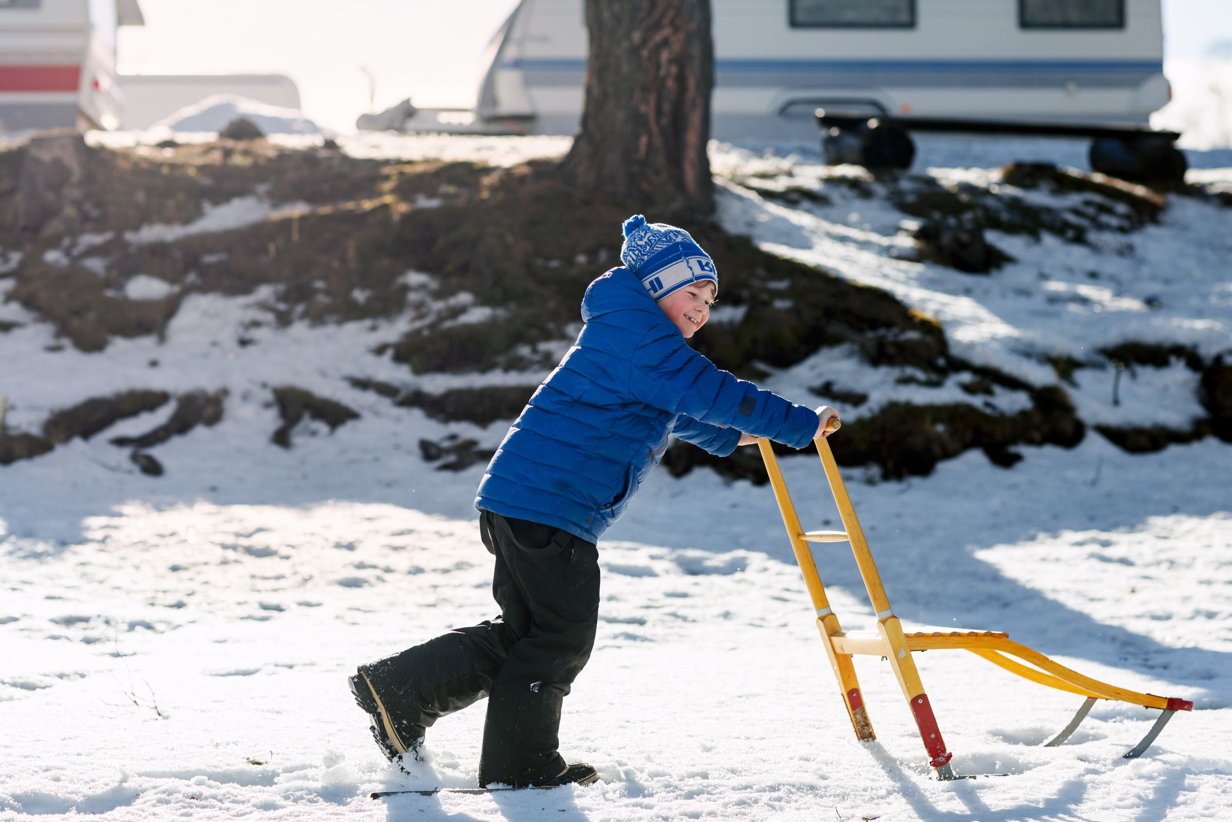 Un niño jugando en la nieve con un trineo amarillo.