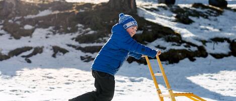 Un niño jugando en la nieve con un trineo amarillo.