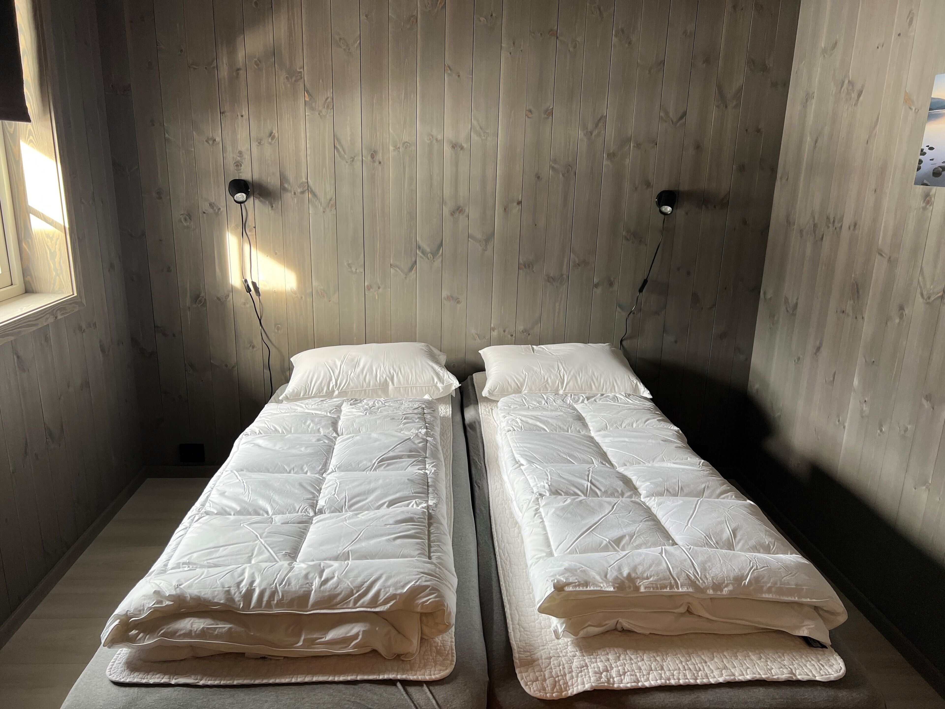 A room with two single beds, wooden walls, and a window on the left.