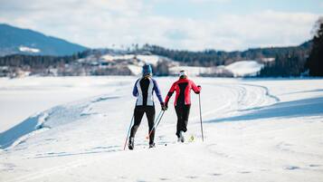Deux personnes pratiquent le ski de fond sur une piste enneigée, avec une chaîne de montagnes en arrière-plan.