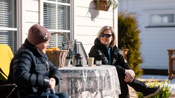 Deux personnes sont assises à une table recouverte d’une nappe en dentelle, avec un panier et un thermos à proximité.