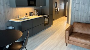 A modern kitchen with dark cabinets, a wooden countertop, and a built-in oven. There is a dining area with a table and chairs, and a brown leather sofa. - Fagernes Camping (Nord-Aurdal)
