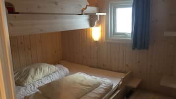 A bunk bed room with wooden walls, a window with curtains, and a small table.
