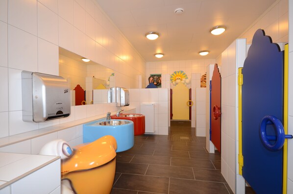 Un baño infantil con lavamanos de colores, un secador de manos y un espejo.